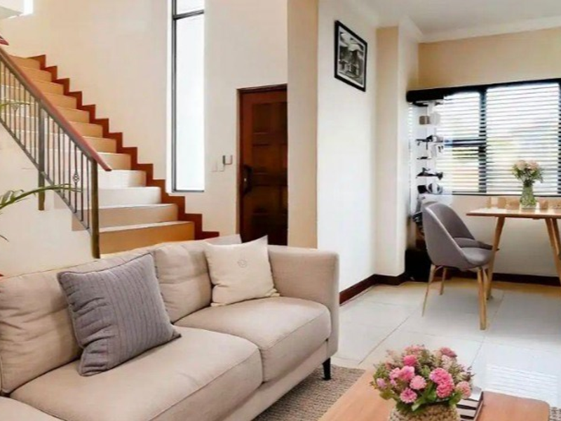 An open-plan living and dining area featuring tiled flooring, a staircase with a metal balustrade, and large windows with venetian blinds.
