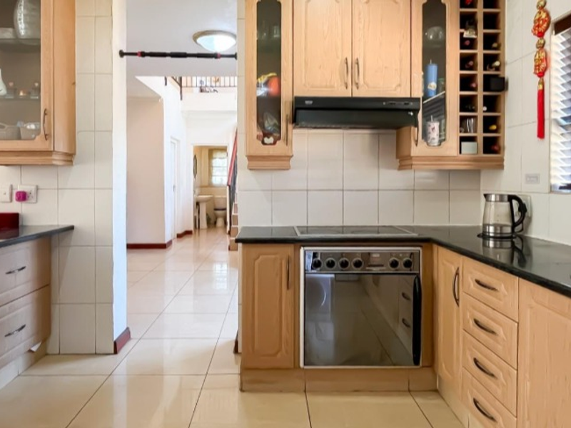 A functional kitchen featuring light wood cabinetry, granite countertops, built-in oven and hob, and tiled flooring, with an open layout leading to the hallway.