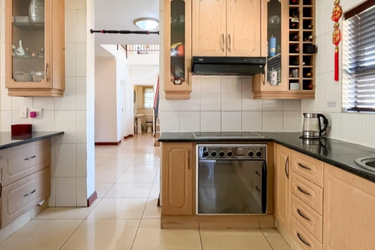 A functional kitchen featuring light wood cabinetry, granite countertops, built-in oven and hob, and tiled flooring, with an open layout leading to the hallway.