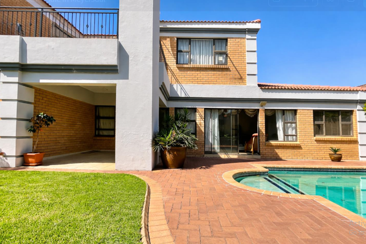 Rear exterior view featuring a swimming pool, brick-paved patio, covered outdoor area, and a balcony with wrought iron railings.