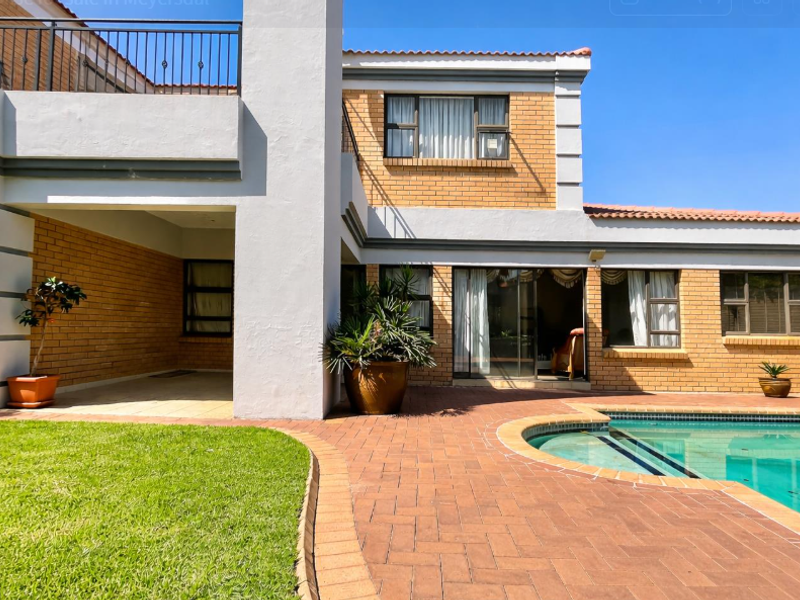 Rear exterior view featuring a swimming pool, brick-paved patio, covered outdoor area, and a balcony with wrought iron railings.