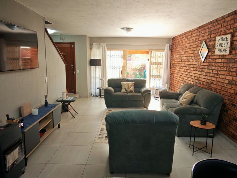 Spacious living room featuring an exposed brick feature wall, neutral tiled flooring, and direct access to the rear patio through sliding glass doors.