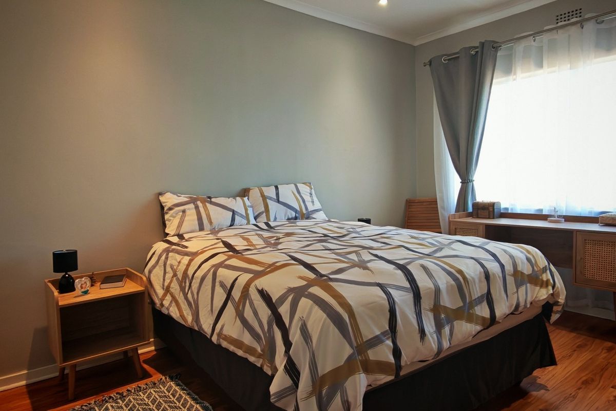 A well-maintained bedroom featuring warm laminate flooring, neutral wall tones, and recessed downlighting, providing a comfortable and inviting living space.