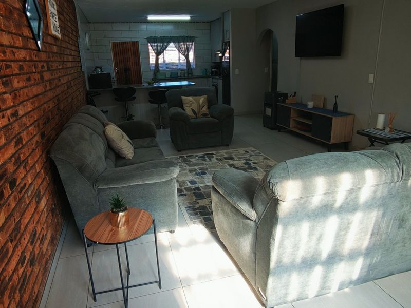 Open plan living area featuring an exposed brick feature wall, tiled flooring, and a breakfast counter connecting to the kitchen space.