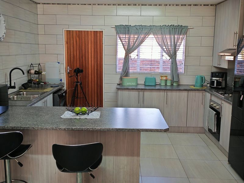 A functional kitchen featuring light wood-grain cabinetry, granite-look countertops, tiled splashbacks, and integrated appliances including an oven and hob.