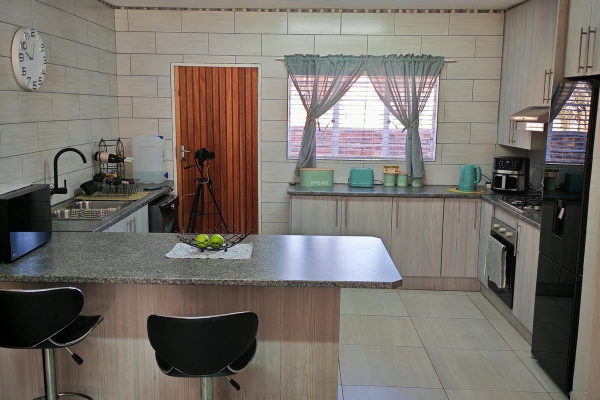 A functional kitchen featuring light wood-grain cabinetry, granite-look countertops, tiled splashbacks, and integrated appliances including an oven and hob.