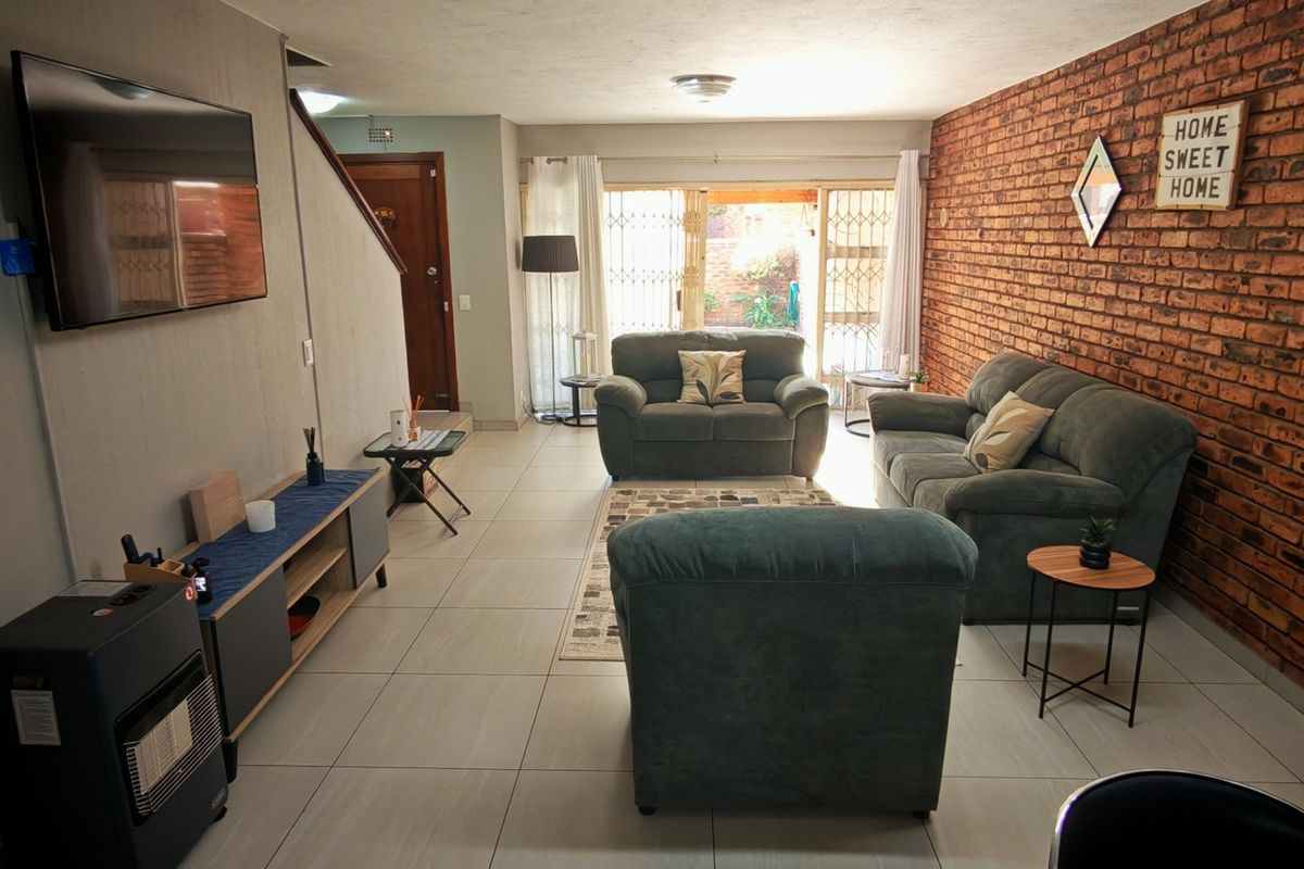 Spacious living room featuring an exposed brick accent wall, neutral tiled flooring, and direct access to the outdoor area through sliding glass doors.