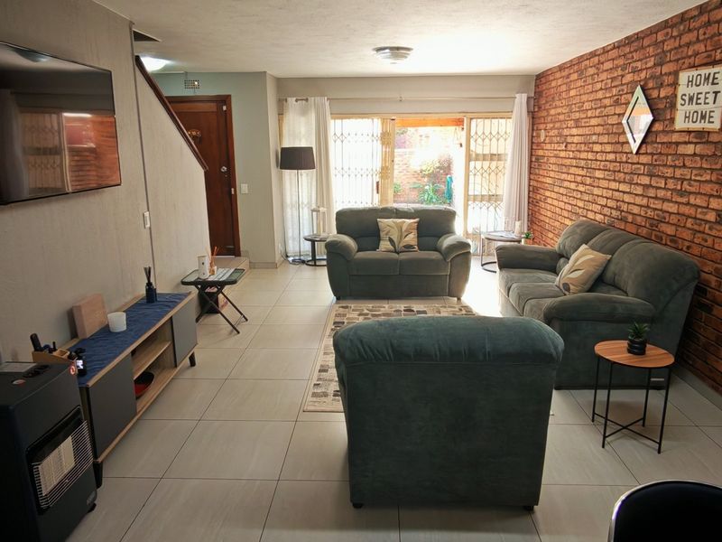 Spacious living room featuring an exposed brick accent wall, neutral tiled flooring, and direct access to the outdoor area through sliding glass doors.