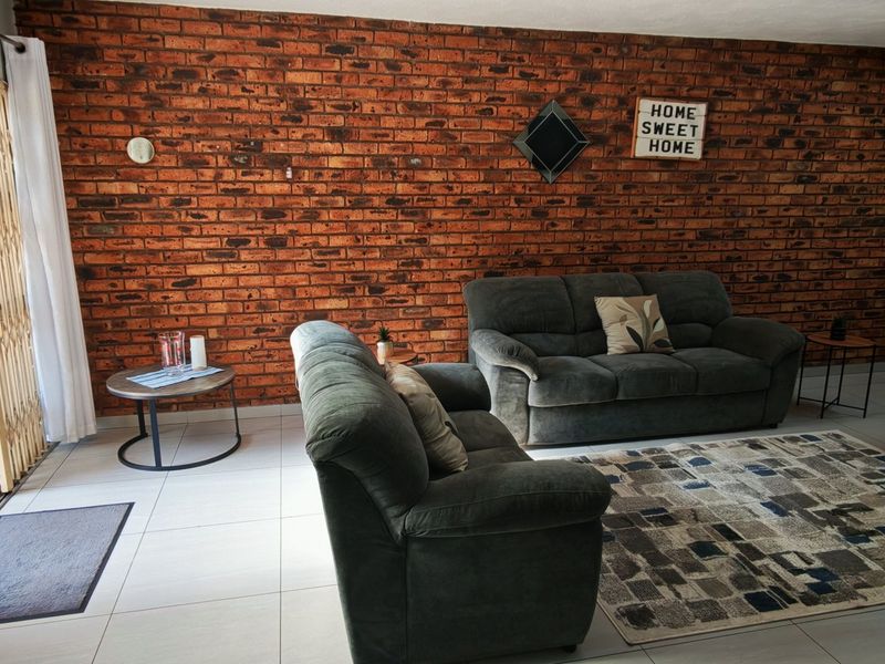 Spacious living area featuring a prominent exposed brick wall, neutral tiled flooring, and direct access to the outdoor patio through sliding glass doors.