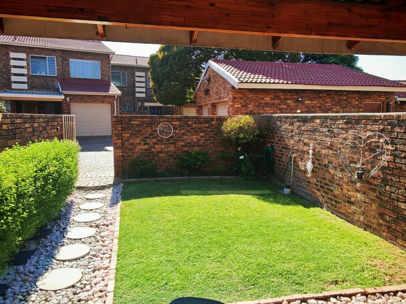 A private rear garden featuring a well-maintained lawn, brick boundary walls, and a paved pathway, viewed from under a timber pergola.