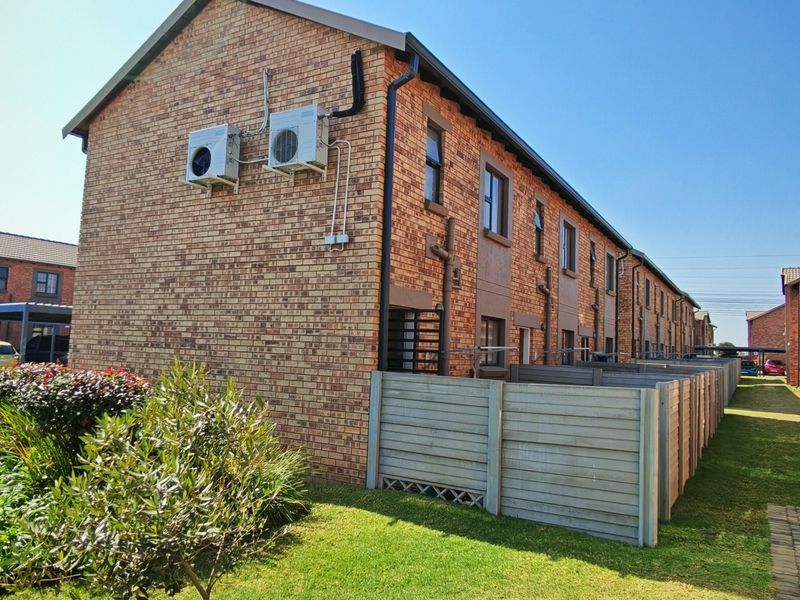 Rear view of a multi-unit townhouse complex featuring face brick construction, external air conditioning units, and private garden spaces with paved walkways.