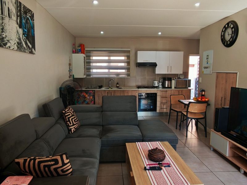 Open-plan living area featuring a modern kitchen with built-in cabinetry, oven, and hob, seamlessly flowing into a comfortable lounge space with tiled flooring.
