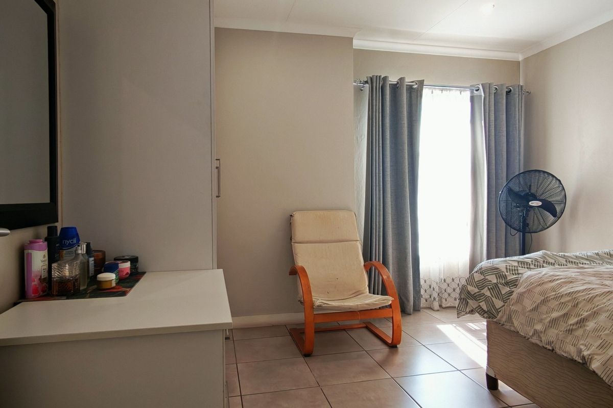 A functional bedroom featuring tiled flooring, a built-in wardrobe, and natural light through a window with curtain rails.