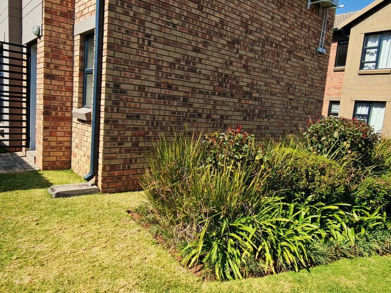 A view of the rear exterior of the townhouse, featuring a face brick facade, a paved walkway, and a well-maintained garden area.