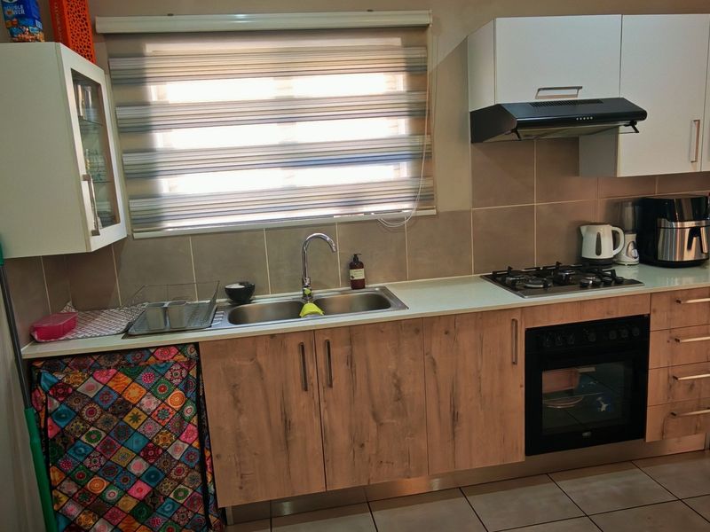 A functional kitchen featuring wood-look cabinetry, a gas hob, built-in oven, extractor fan, and a stainless steel sink with tiled backsplash.