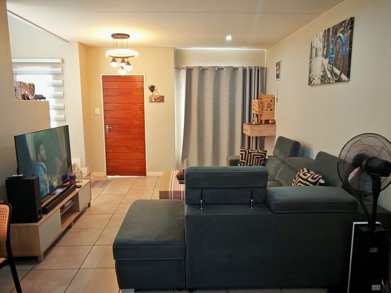 A comfortable living room featuring tiled flooring, a solid wooden front door, and neutral wall finishes, providing a functional and welcoming space.