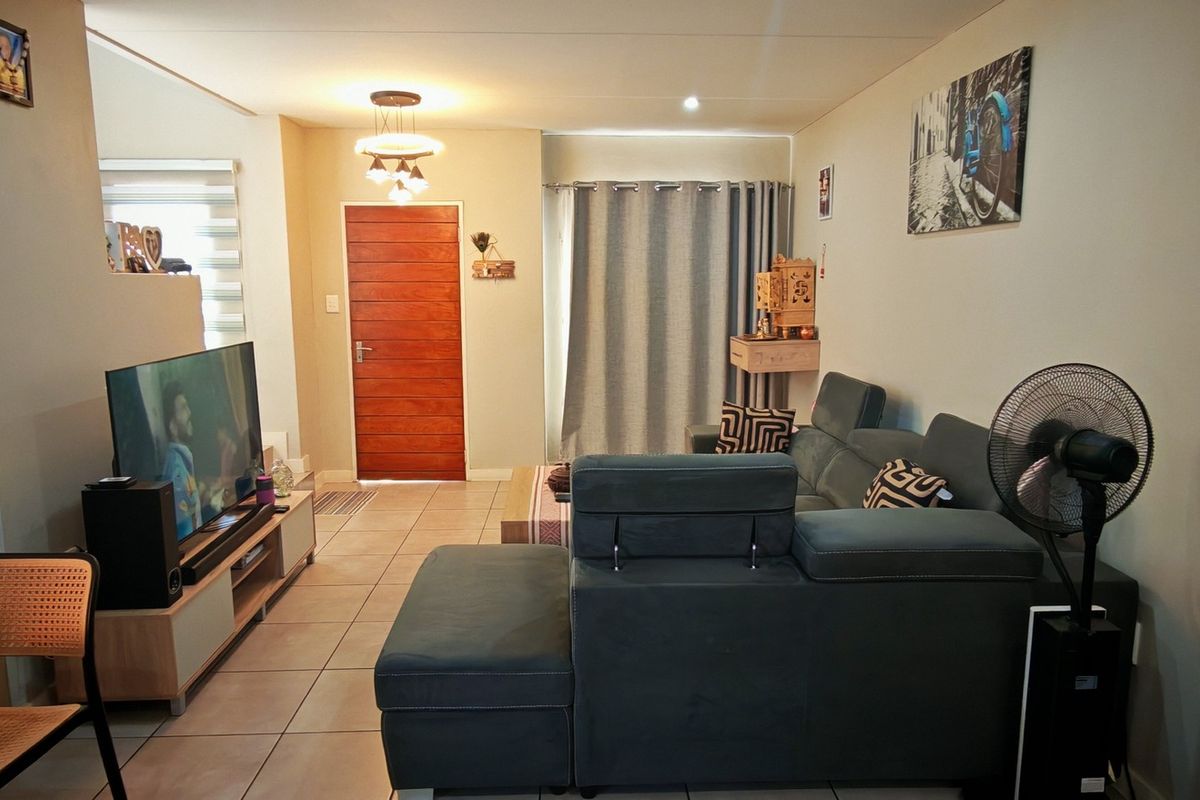 A comfortable living room featuring tiled flooring, a solid wooden front door, and neutral wall finishes, providing a functional and welcoming space.