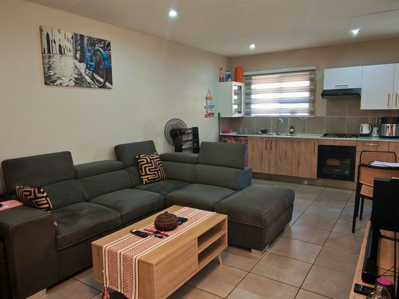 Open-plan living area featuring a functional kitchen with built-in cabinetry, oven, and hob, seamlessly flowing into the lounge space with tiled flooring throughout.