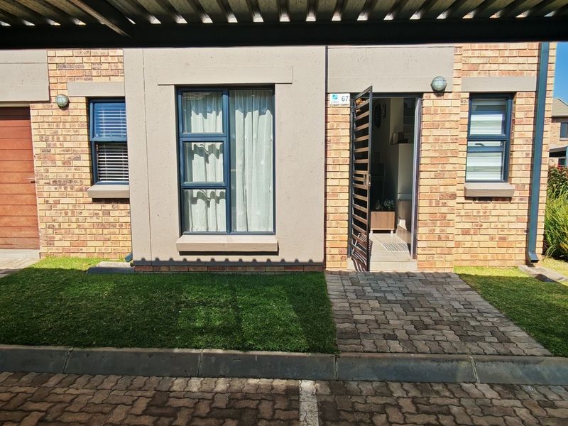 Front elevation of a modern townhouse featuring brick facade, aluminium windows, paved entrance path, and a covered carport area.