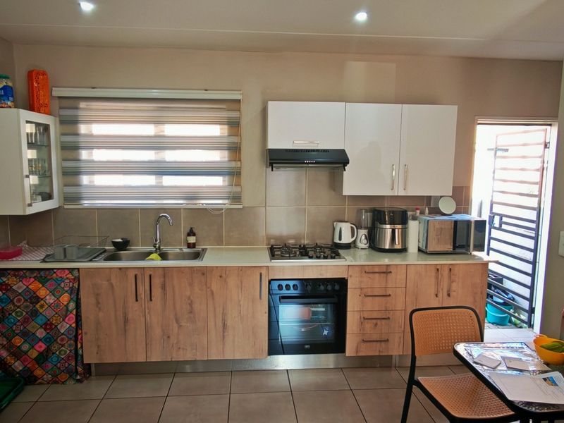 A functional kitchen featuring wood-look cabinetry, a gas hob with extractor, built-in oven, and tiled flooring, with direct access to an exterior area.