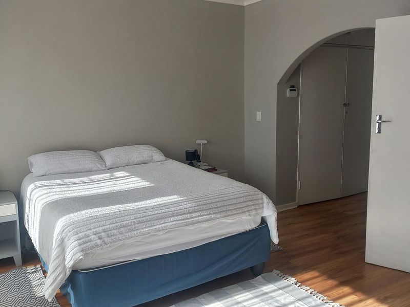 A bedroom featuring laminate flooring, an arched entryway leading to built-in cupboards, and neutral wall tones.