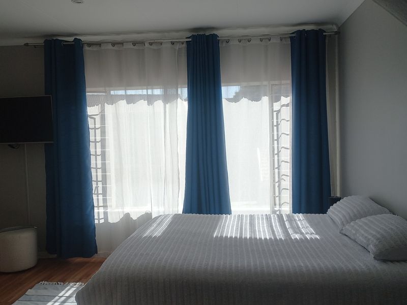 A bedroom featuring timber flooring, recessed ceiling lighting, and large windows dressed with curtains.