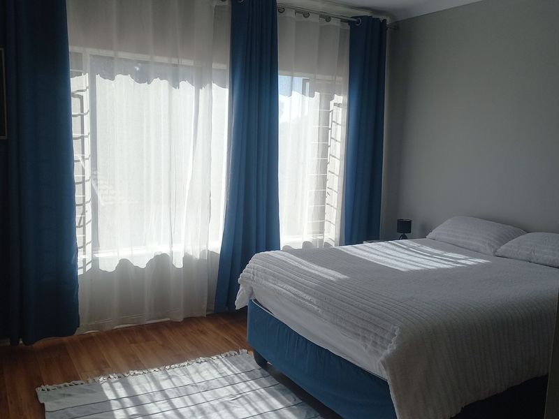 A well-lit bedroom featuring laminate flooring and large windows with security bars, providing a comfortable and functional living space.