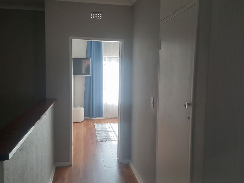 A view of a hallway leading into a bedroom, featuring a wooden handrail and neutral wall finishes.