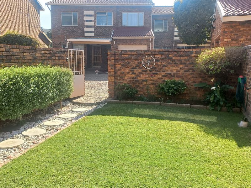 A well-maintained rear garden featuring a manicured lawn, brick boundary walls, and a paved pathway leading to the townhouse entrance.