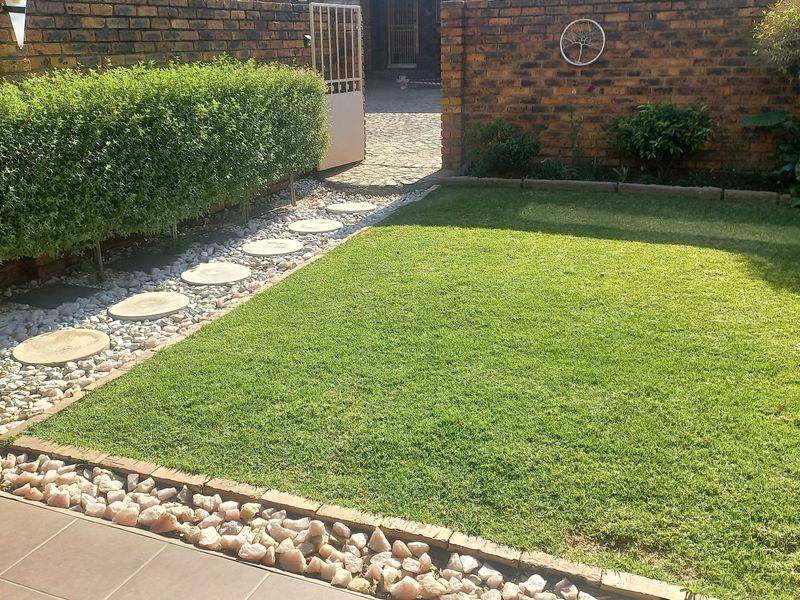 A well-maintained private garden featuring a manicured lawn, stone pathway, and brick boundary walls, providing a neat and functional outdoor space.