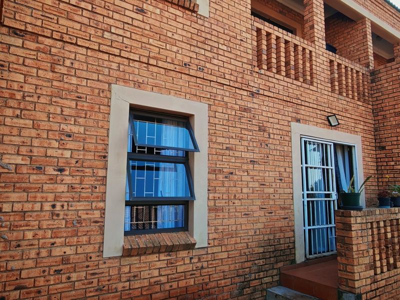 Rear exterior view of a face brick townhouse featuring a balcony with brick balustrade, security gates, and top-hung windows.