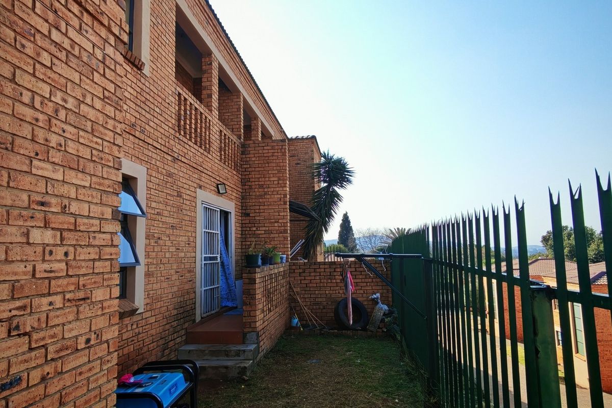 Rear exterior view of a face brick townhouse featuring a balcony, security gate, and metal perimeter fencing.