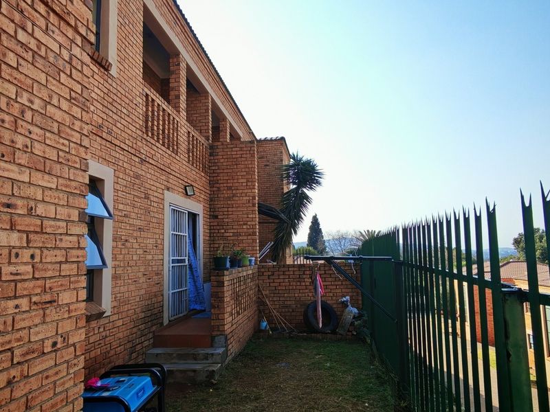 Rear exterior view of a face brick townhouse featuring a balcony, security gate, and metal perimeter fencing.