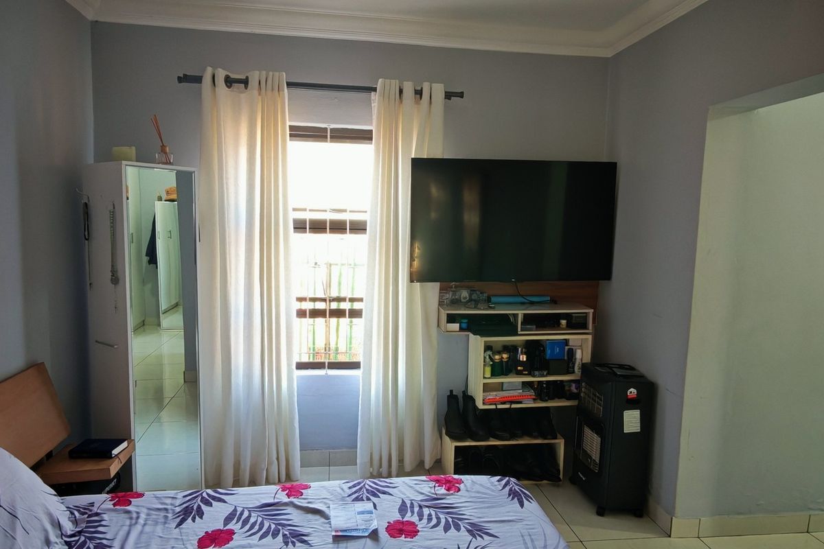 A functional bedroom featuring tiled flooring, neutral wall finishes, and a window with curtain treatments.