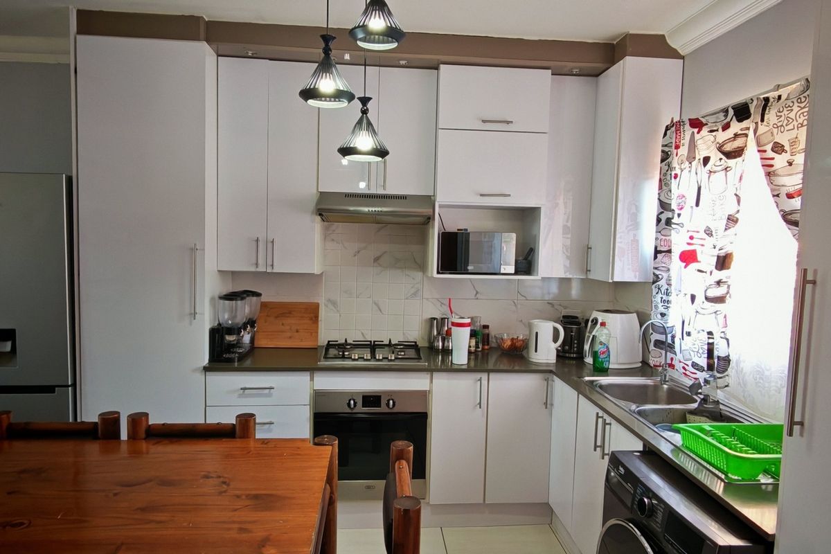 A functional kitchen featuring white cabinetry, a gas hob, built-in oven, extractor fan, and a double sink with tiled backsplash.