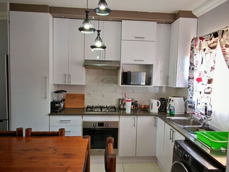 A functional kitchen featuring white cabinetry, a gas hob, built-in oven, extractor fan, and a double sink with tiled backsplash.