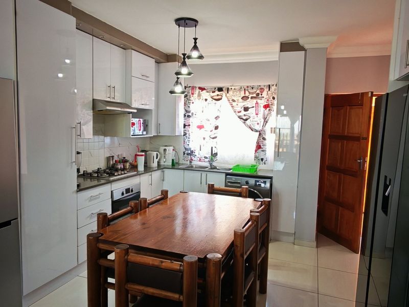A functional kitchen featuring modern white cabinetry, a gas hob with extractor, under-counter oven, and tiled flooring, providing a clean and practical cooking space.