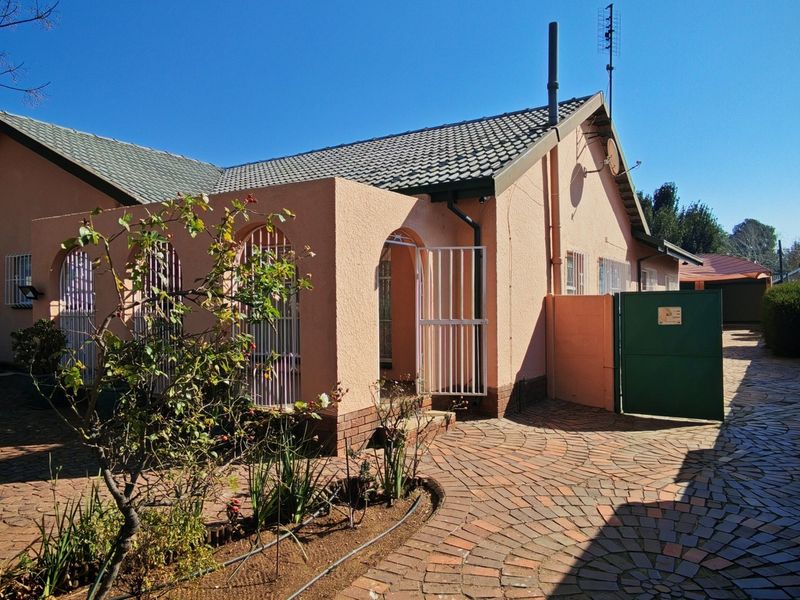 Front elevation of a single-story house featuring a tiled roof, arched porch entrance, and extensive brick-paved driveway with secure gated access.