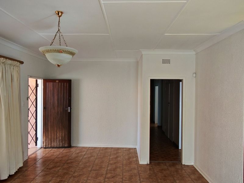 An empty living area featuring tiled flooring, timber paneling, and a decorative ceiling, providing a neutral canvas for potential interior updates.