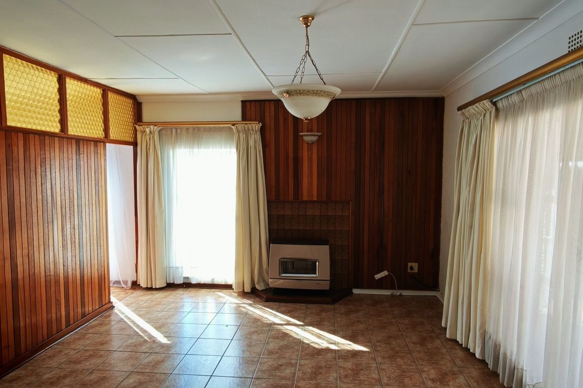 Spacious living area featuring timber wall paneling, tiled flooring, and a built-in gas fireplace, offering a dated aesthetic ready for modern renovation.