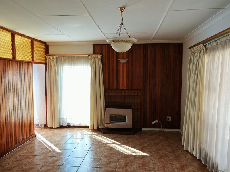 Spacious living area featuring timber wall paneling, tiled flooring, and a built-in gas fireplace, offering a dated aesthetic ready for modern renovation.