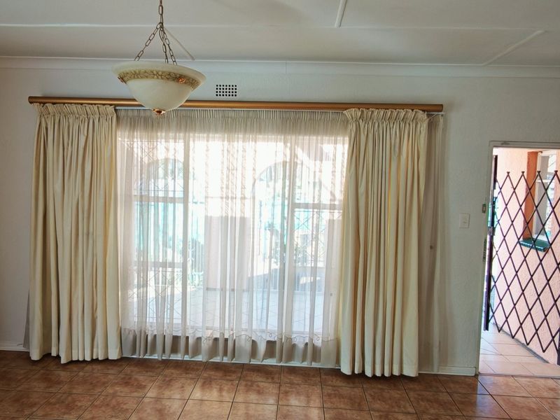 A spacious, empty living area featuring tiled flooring, a central light fixture, and direct access to an outdoor space through a security gate.