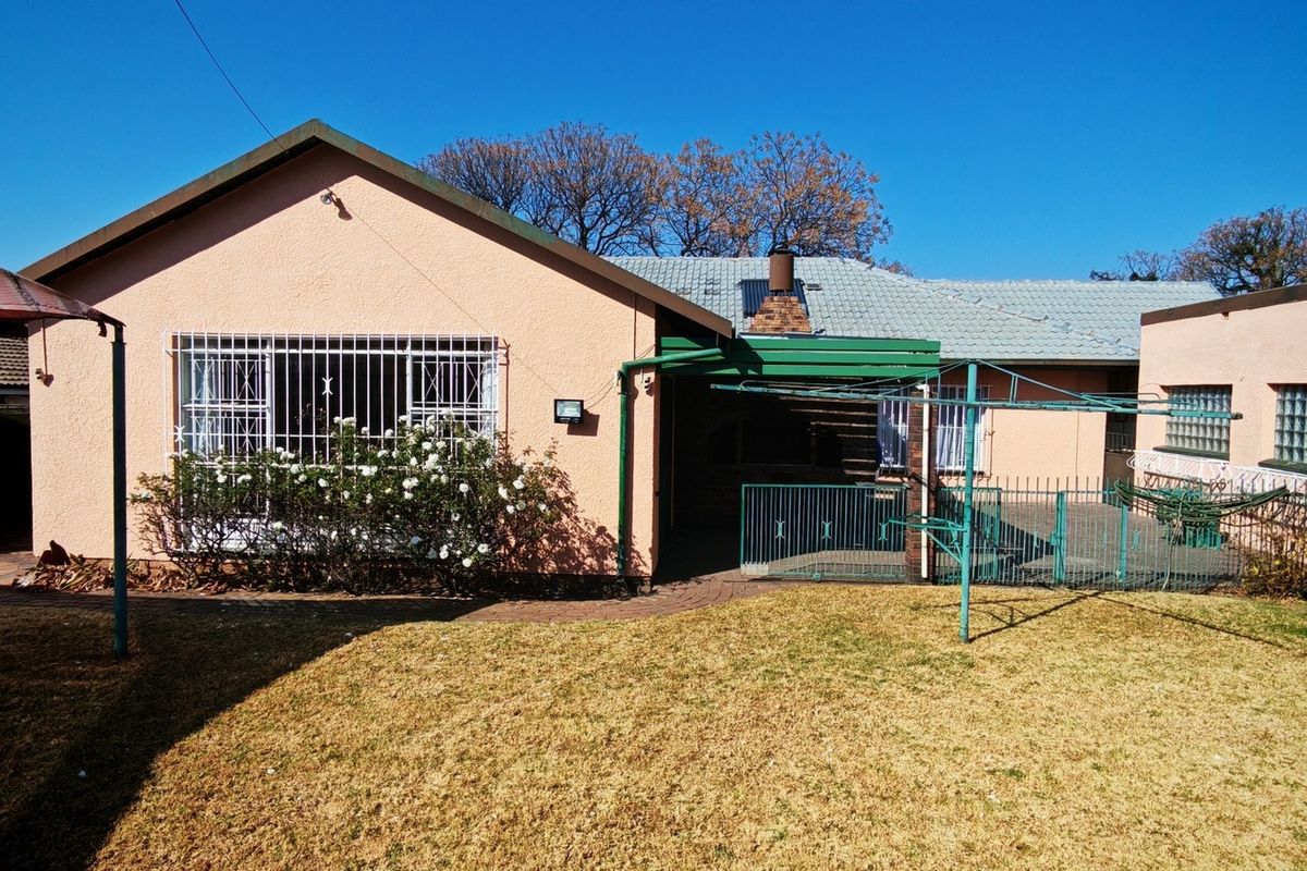 Rear view of the house featuring a paved patio area, security bars on windows, and a small garden space.