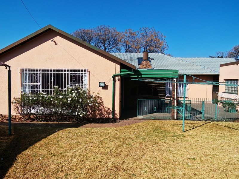 Rear view of the house featuring a paved patio area, security bars on windows, and a small garden space.