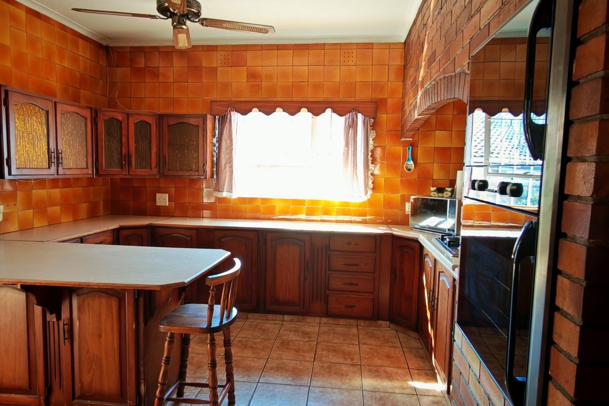 A traditional kitchen featuring extensive wooden cabinetry, ceramic wall and floor tiles, and a distinctive brick archway detail.