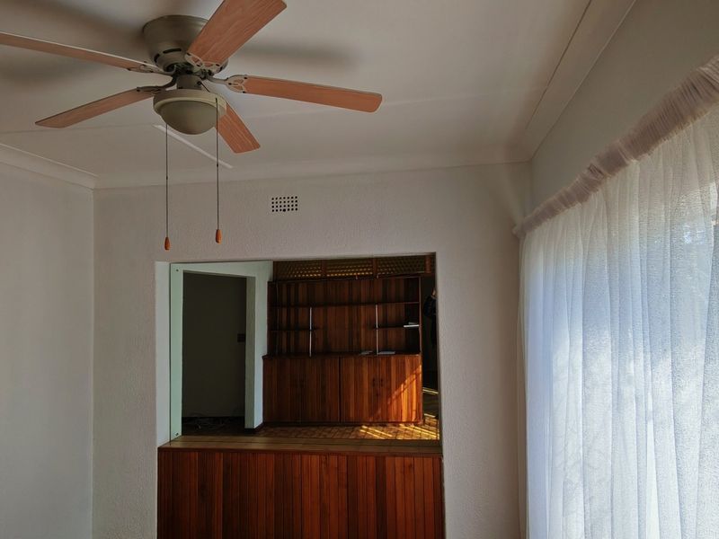 A bright living area featuring a ceiling fan, cove cornicing, and a built-in wooden serving hatch connecting to an adjacent room.