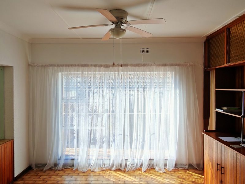 A bright living room featuring parquet flooring, a ceiling fan, and extensive built-in wooden cabinetry and shelving units.