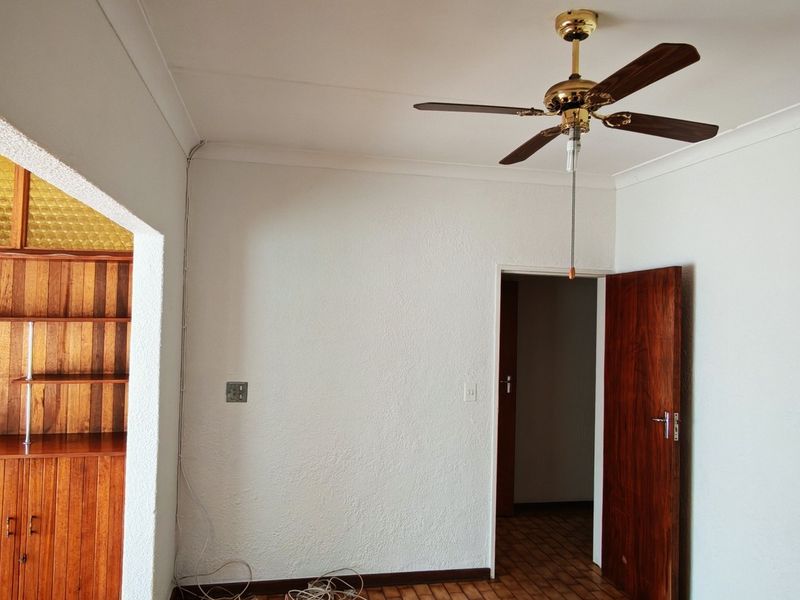 An empty living area featuring a ceiling fan, coved cornicing, and built-in wooden cabinetry visible through an adjacent doorway.