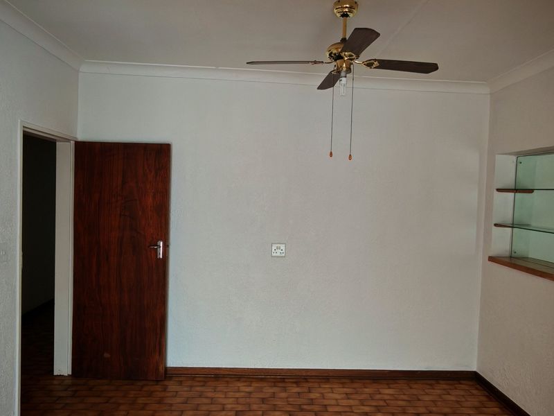 An empty living room featuring parquet flooring, a ceiling fan, and a built-in glass display shelf.