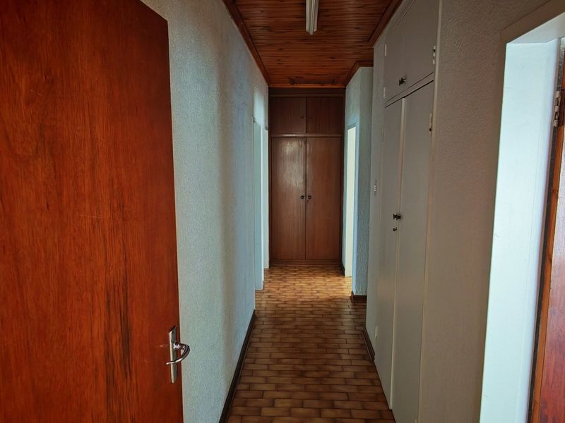 A functional hallway featuring built-in storage cupboards, a timber-paneled ceiling, and tiled flooring, providing access to various rooms within the home.